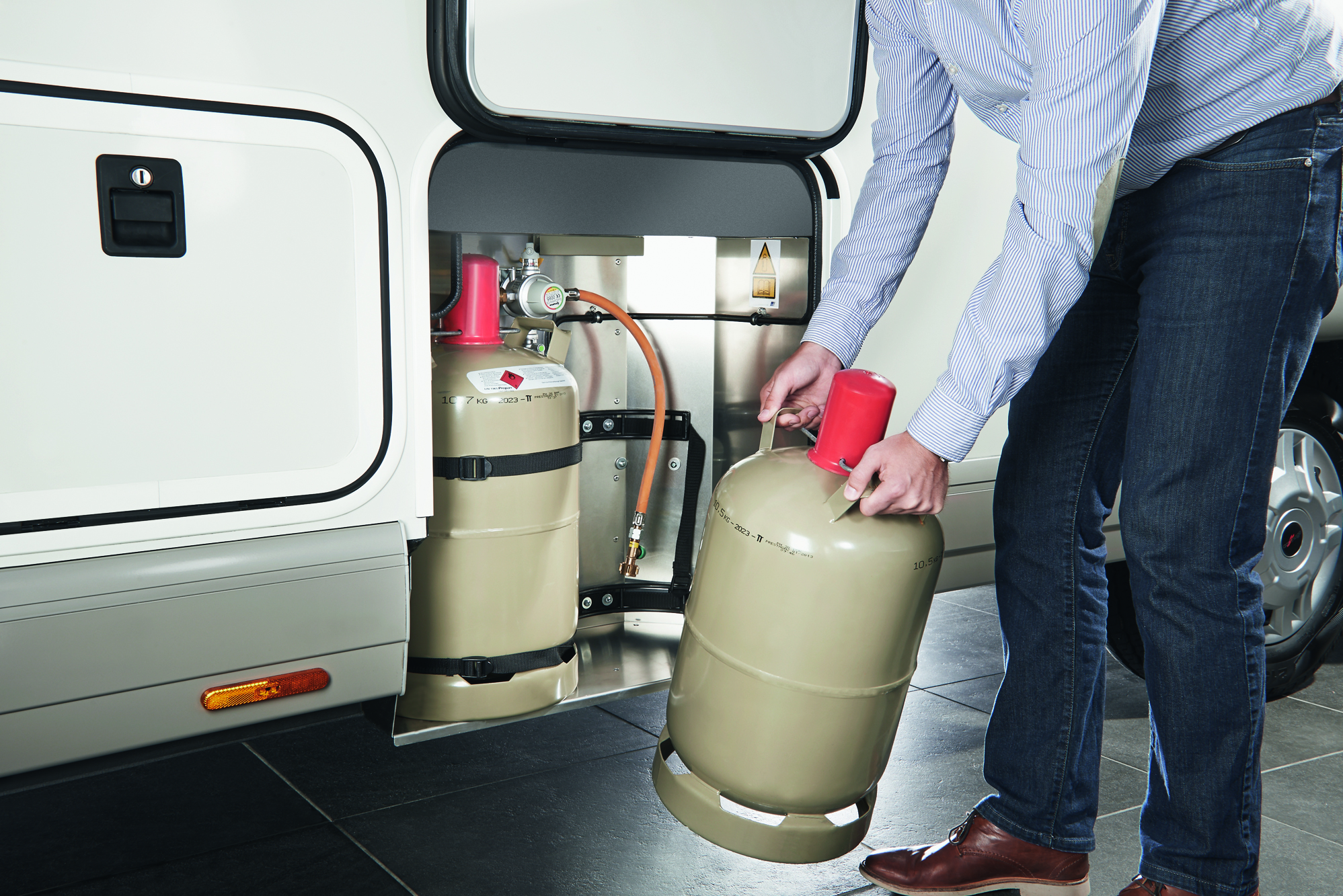 Person wechselt eine Gasflasche im Gasflaschenkasten eines Carthago c-line T