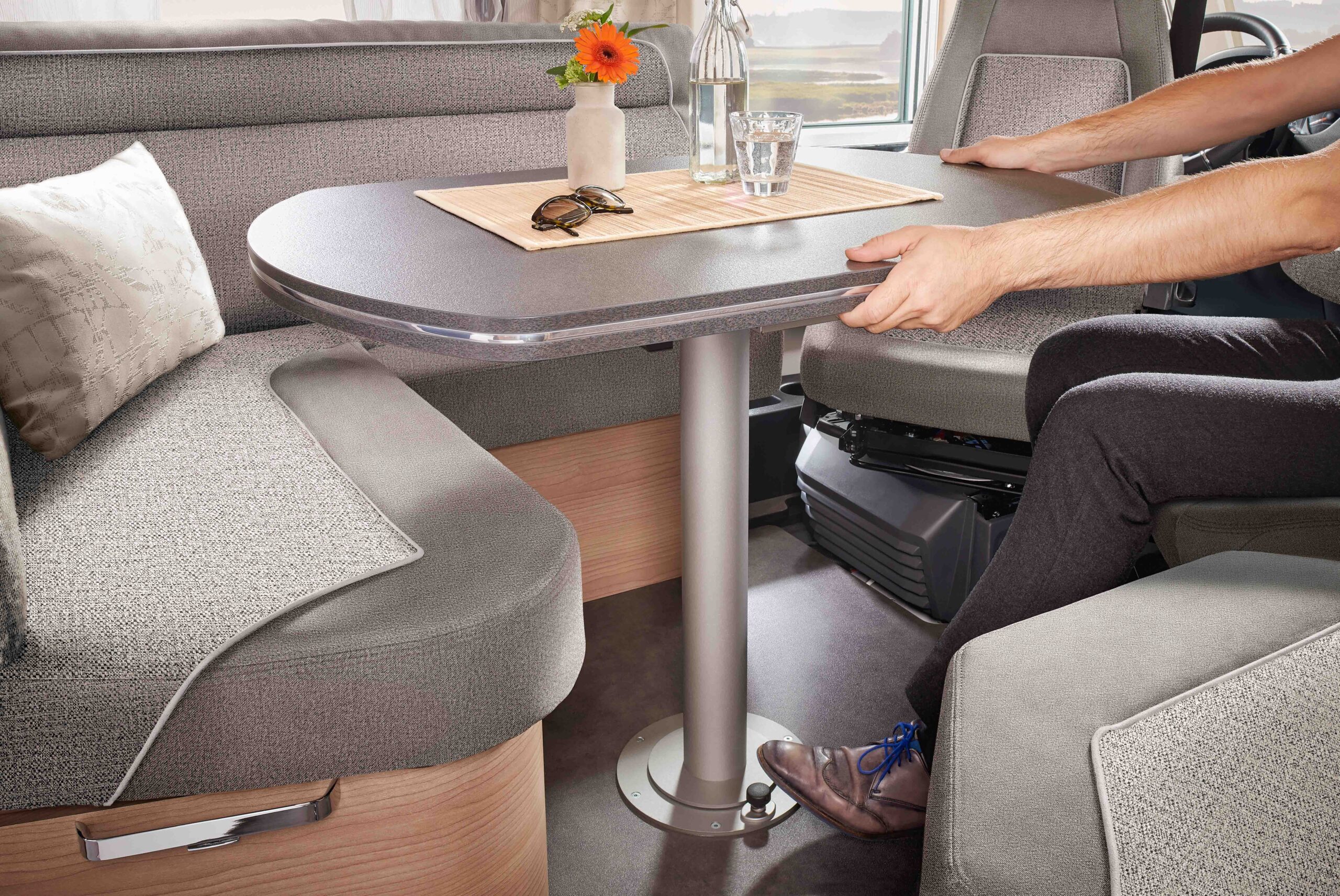 Sitzgruppe mit Tisch in einem Malibu Reisemobil, eine Person verstellt den Tisch