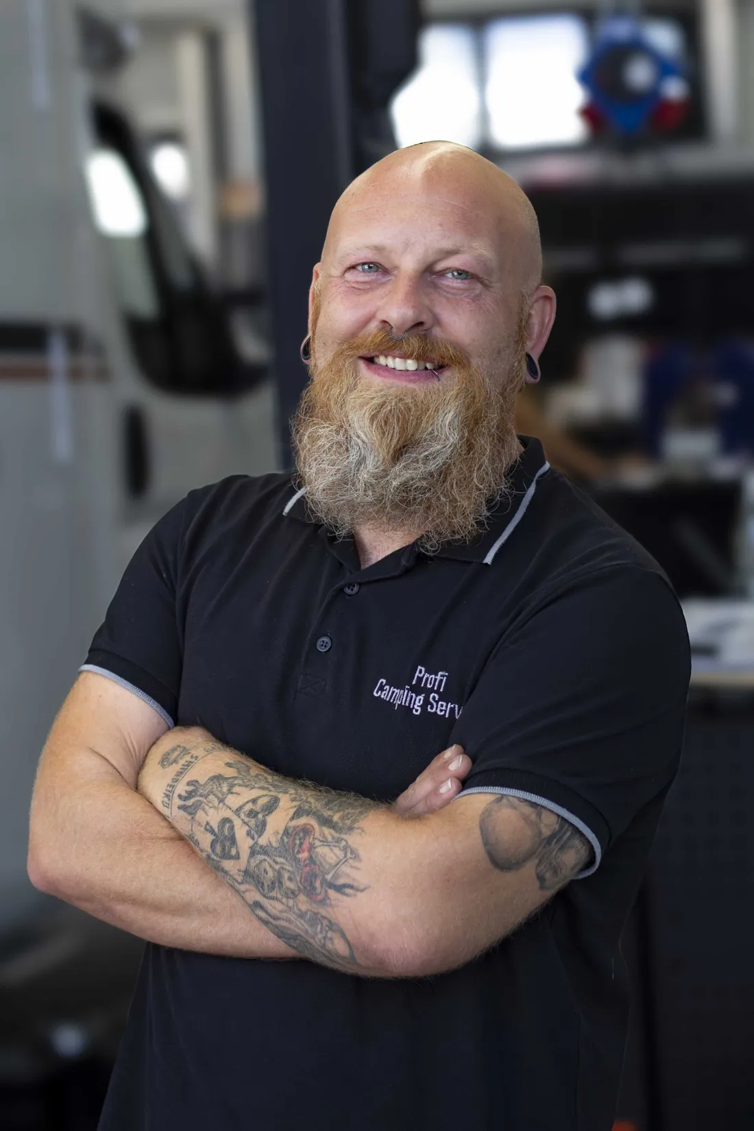Mitarbeiter des Profi-Camping-Service mit verschränkten Armen im schwarzen Poloshirt mit Firmenstickerei, er lächelt in die Kamera