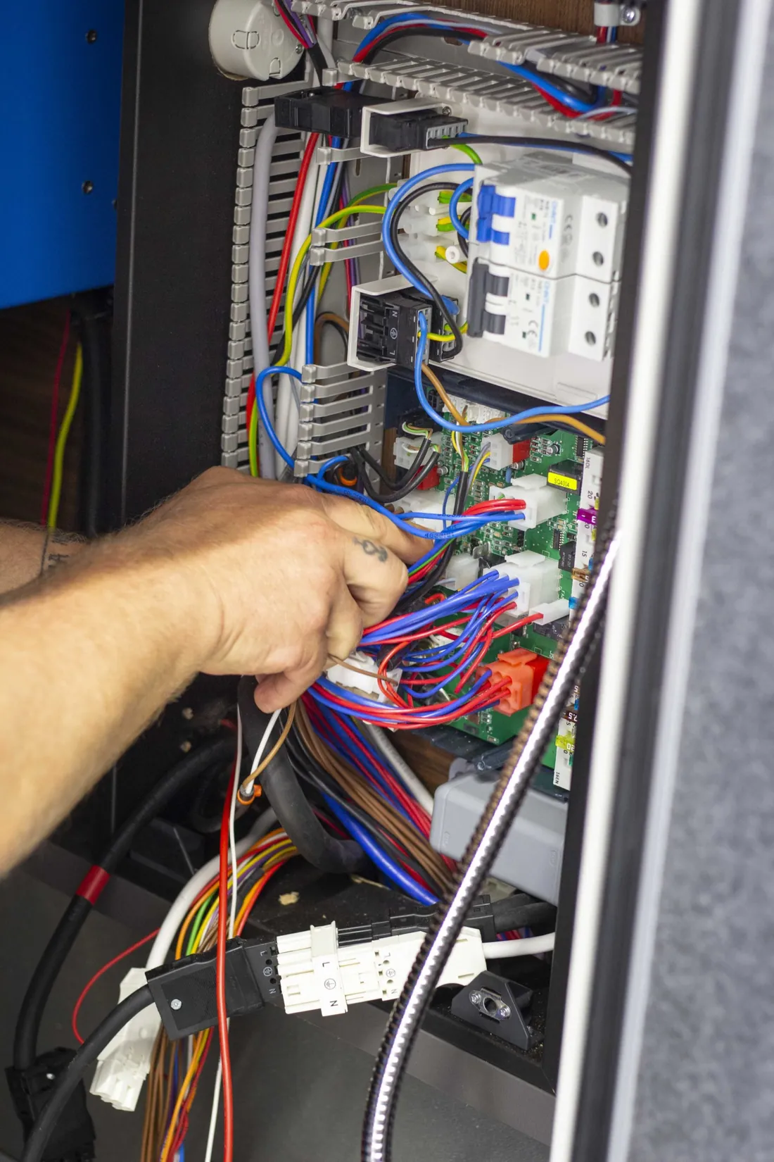 Hand eines Technikers greift in den Kabelbaum der Bordelektronik eines Reisemobils