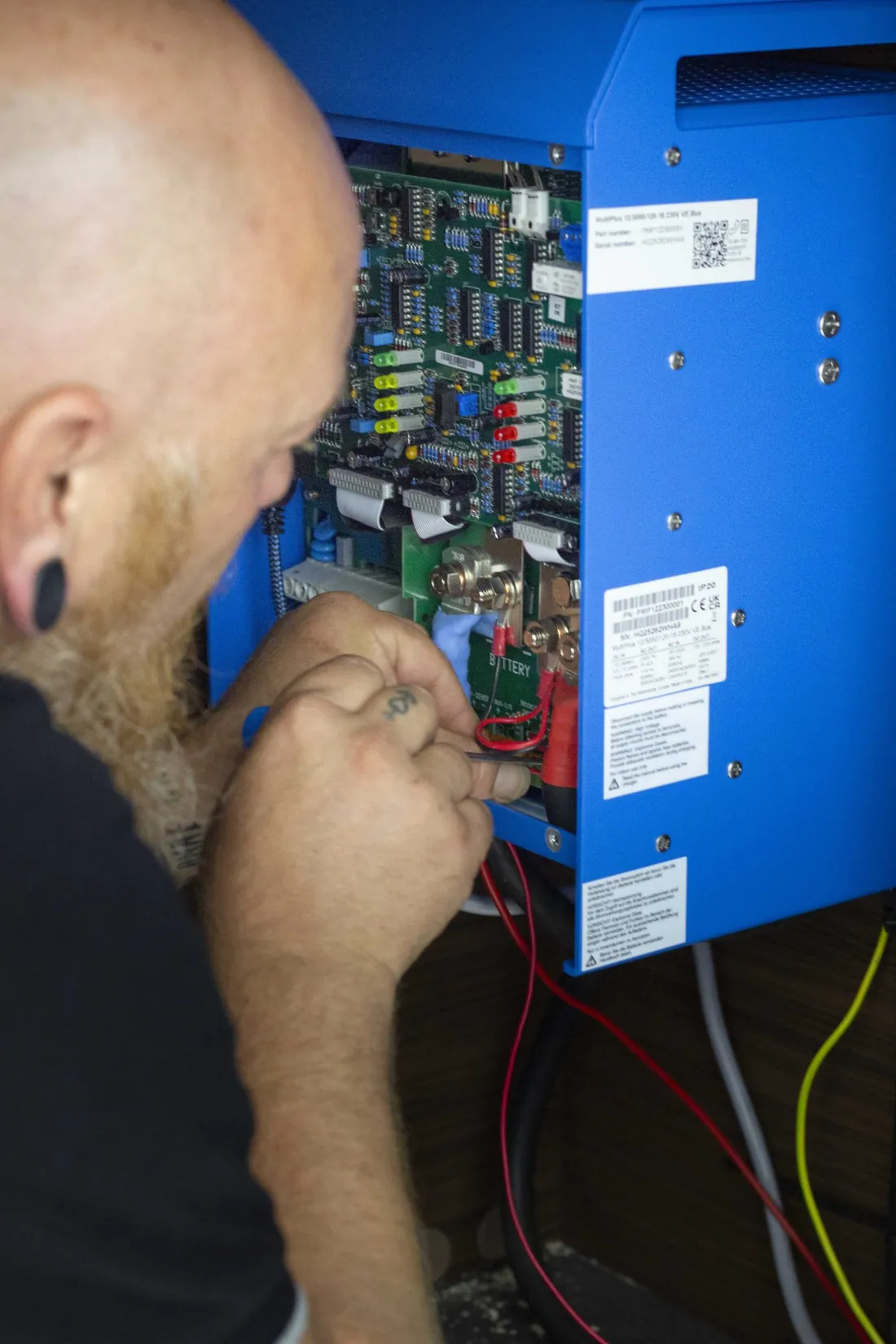 Techniker des Profi-Camping-Service arbeitet mit einem Schraubendreher an den Anschlüssen eines blauen Wechselrichters